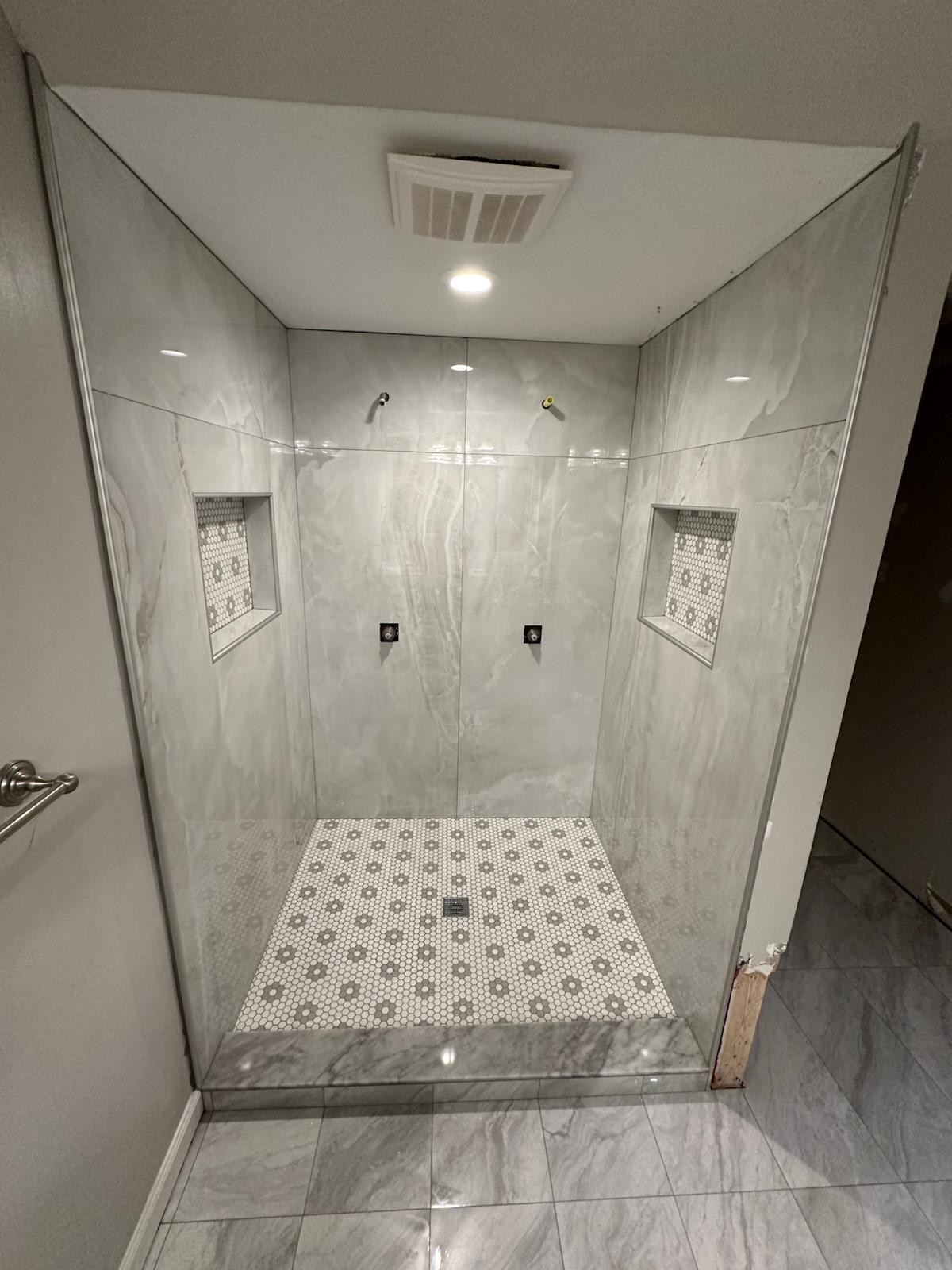 Frameless glass shower with marble-look tile and two matching mosaic niches